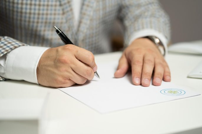 Osoba podpisuje dokument długopisem przy biurku.